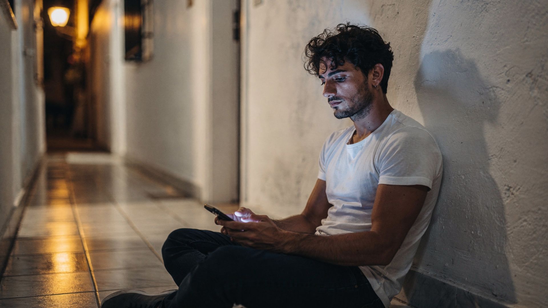 Racconti gay coming out: un giovane uomo al telefono di notte, seduto in corridoio